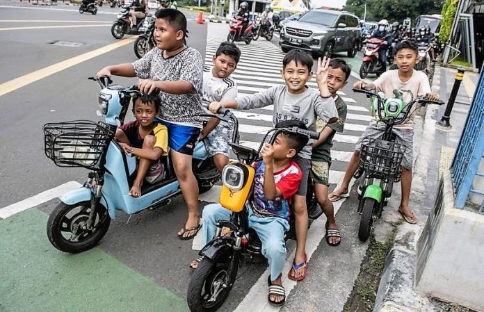 Sejumlah anak-anak menggunakan sepeda listrik di jalan raya.