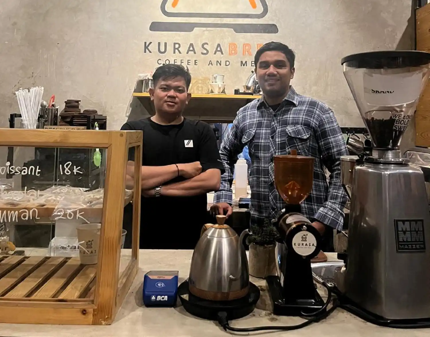 Dua orang berdiri di area barista Kurasa Coffee Bandung, menunjukkan konsep coffee shop kreatif dan kekinian untuk anak muda.