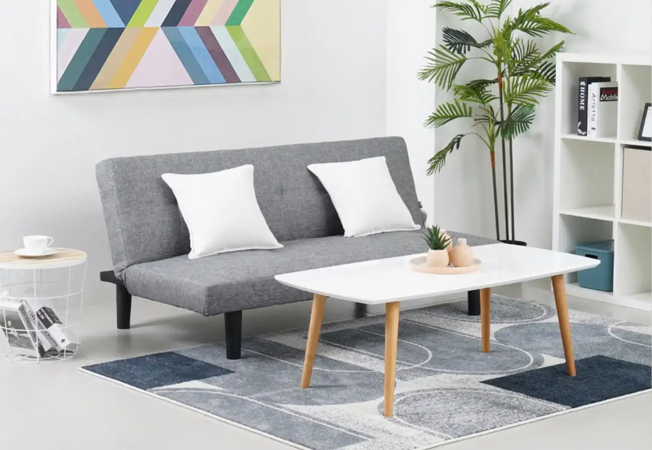 Sofa bed minimalis kain abu-abu di ruang tamu modern dengan meja kayu dan dekorasi tanaman.