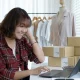 Seorang pelaku UMKM sedang mengelola penjualan online di depan laptop, dikelilingi paket produk siap kirim.